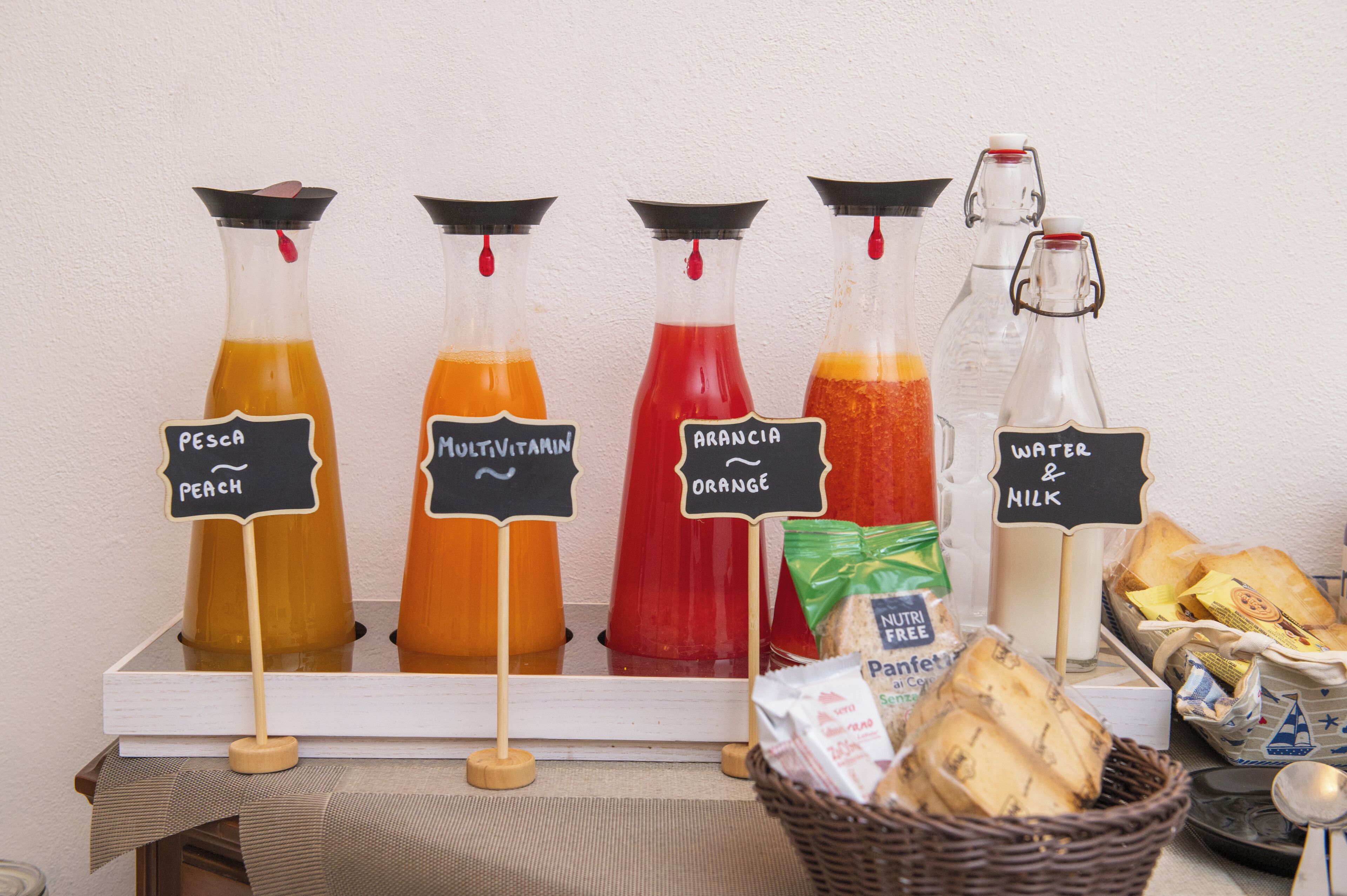 A beverage station with labeled bottles of peach, multivitamin, orange, and water & milk.