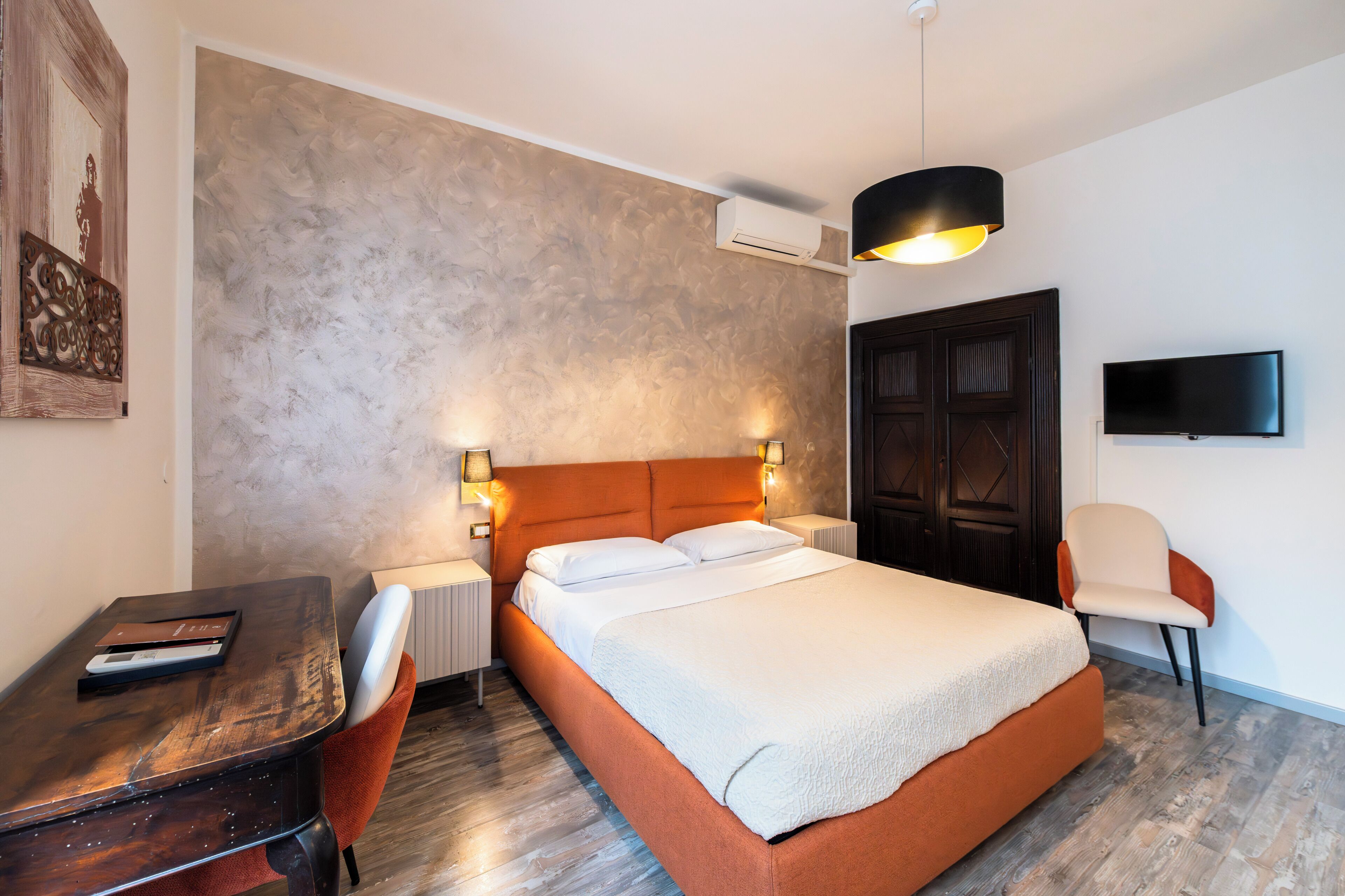 Een moderne hotelkamer met een groot bed, een bureau, een stoel, een televisie en een wandairconditioner.