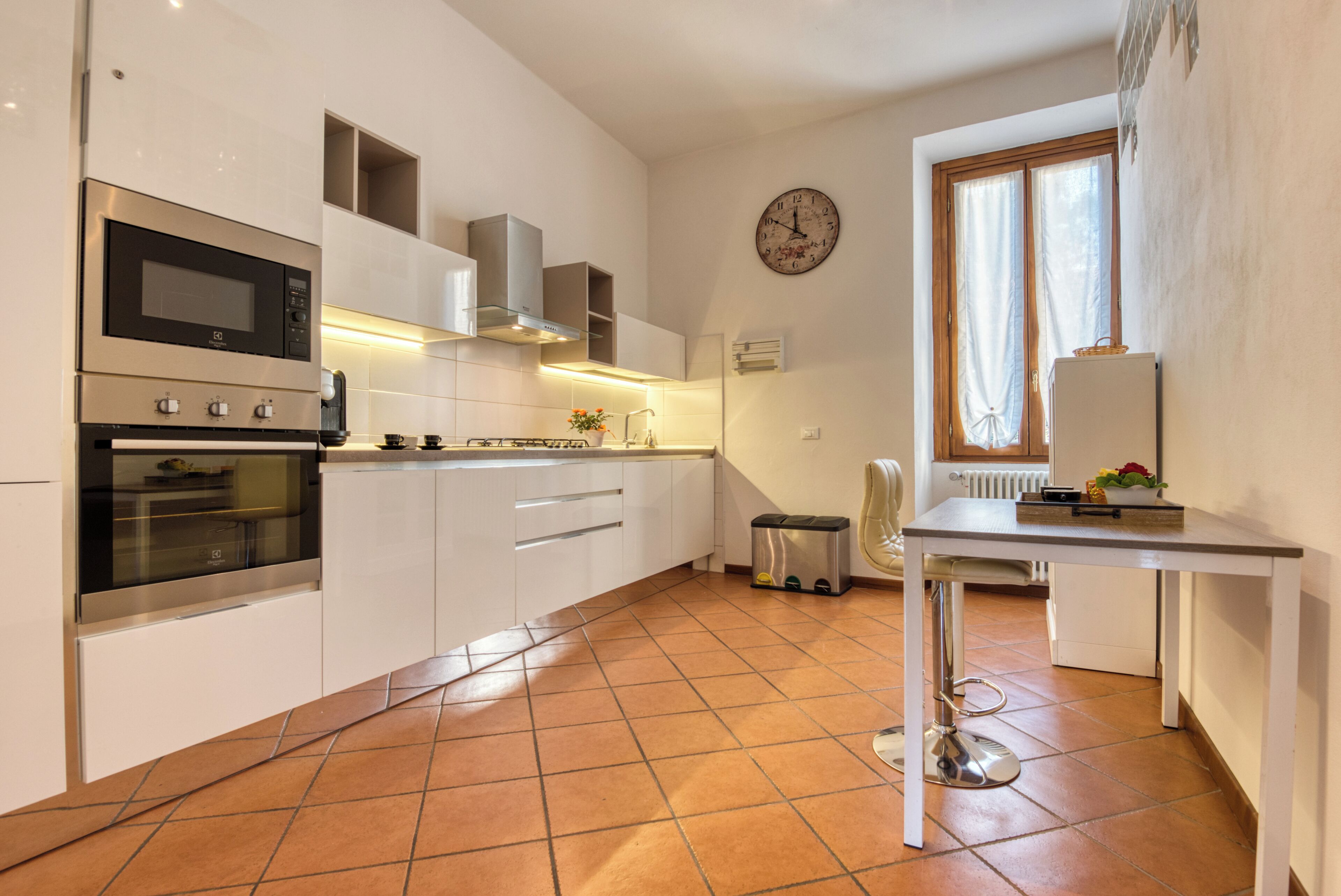 Une cuisine moderne avec des armoires blanches, un four en acier inoxydable, un four à micro-ondes et une table à manger avec une chaise.