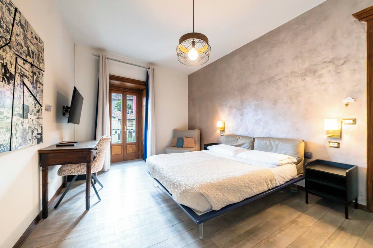 A bedroom with a bed, bedside tables, a desk, a chair, a television, and a door leading to an outdoor area.