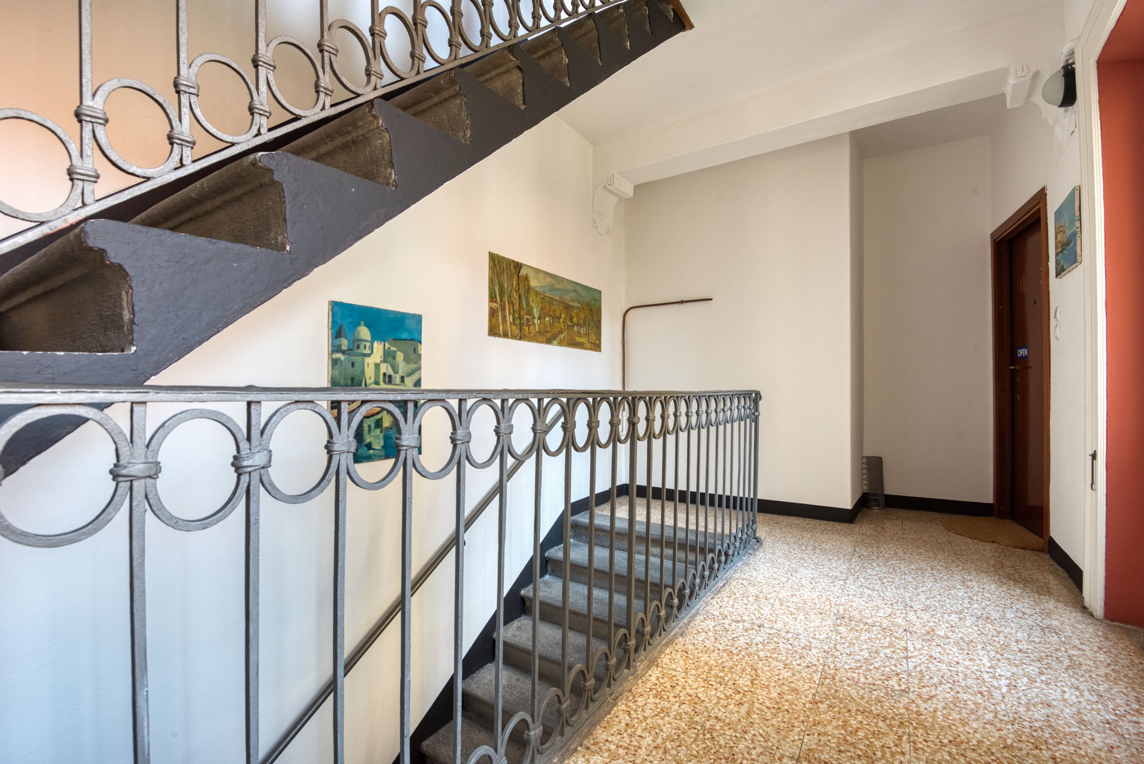 Una escala amb baranes de metall ornamentades, un terra endollit i dos quadres a la paret.