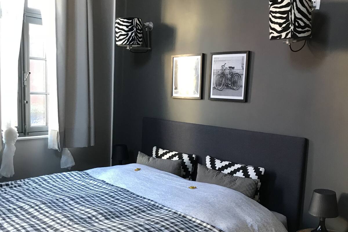A modern bedroom with a large bed, a bedside table, and a window with curtains.