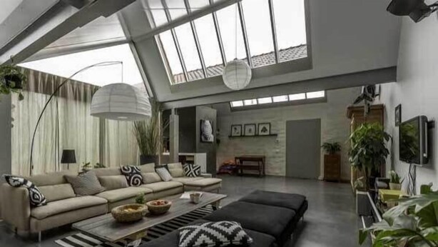 A spacious living room with a high ceiling, a sectional sofa, a coffee table, and a large window providing natural light.