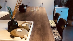 A modern dining area with a wooden table, clear glasses, a black teapot, and a decorative rock arrangement.