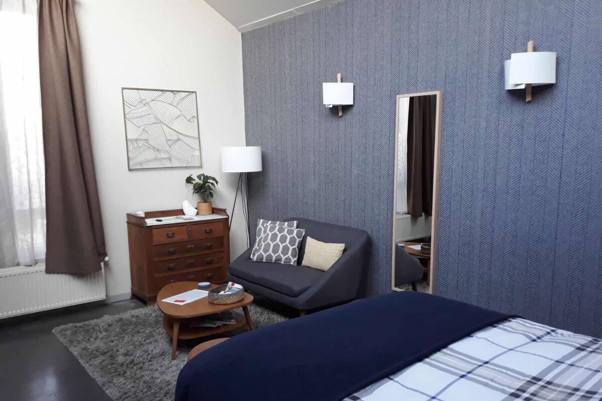 A modern hotel room with a large bed, a sofa, a small coffee table, a dresser, and a mirror.