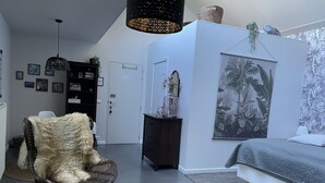 A modern living room with a large furry chair, a grey sofa, a wicker basket with books, and a wall with a tropical plant mural.