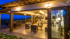 An outdoor patio with wicker furniture, a dining table, and a view of the ocean. - Pousada Manacá Parque (Porto Seguro)