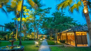 A pathway leading to a building with a tiled roof, surrounded by palm trees and a fountain. - Pousada Manacá Parque (Porto Seguro)