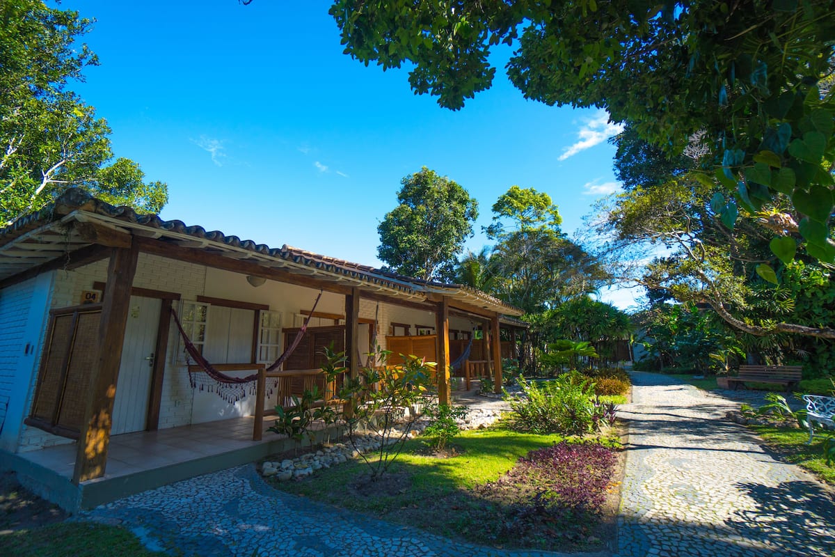 A traditional house with a tiled roof, a porch, and a garden with various plants and a bench.