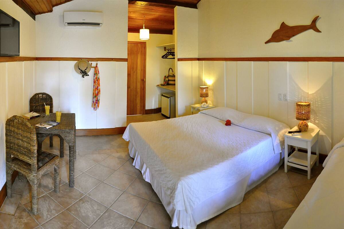 A hotel room with a bed, a desk, and a chair. There is a wall-mounted air conditioner and a wall decoration of a fish.
