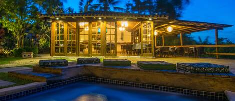 A poolside area with a covered seating area, a pool, and a building with large windows.