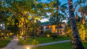 A two-story building with a paved pathway leading to the entrance, surrounded by lush greenery and palm trees. - Pousada Manacá Parque (Porto Seguro)