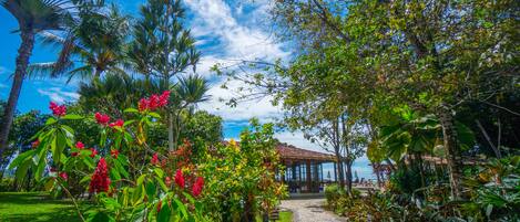 A garden pathway leading to a wooden gazebo with a view of the sea.