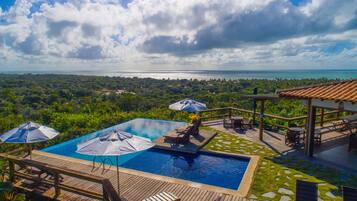 Uma área de piscina com duas piscinas, guarda-sóis e espreguiçadeiras.