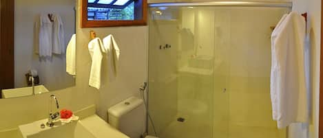 A bathroom with a glass-enclosed shower, a white sink, a toilet, and a mirror with towels hanging on the wall.