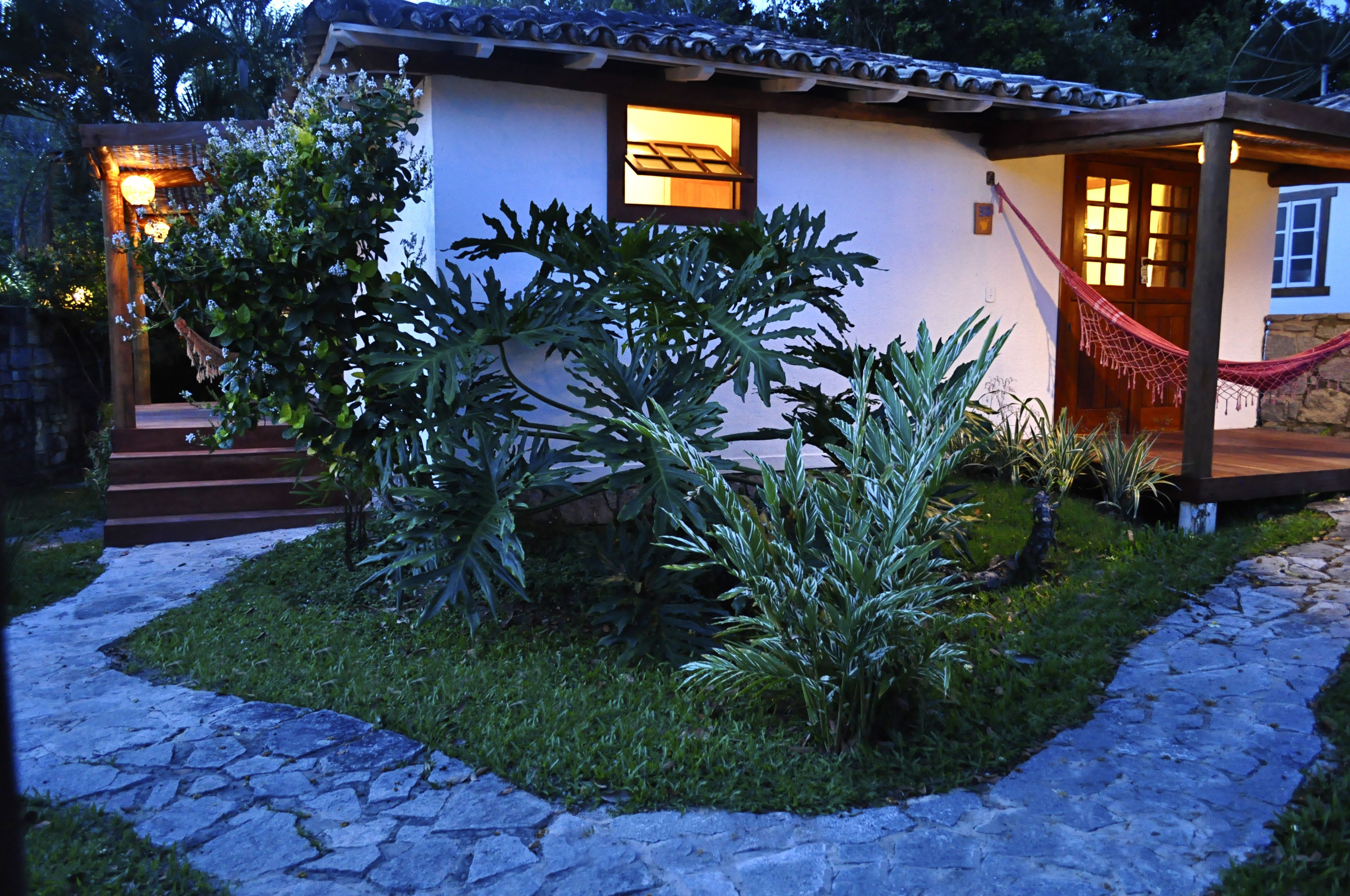 A house with a stone pathway, a hammock, and a small garden with various plants.