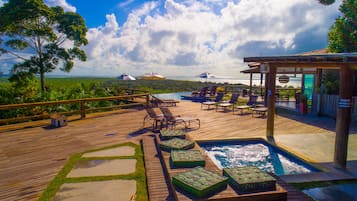 A wooden deck with lounge chairs, a hot tub, and a view of the ocean.