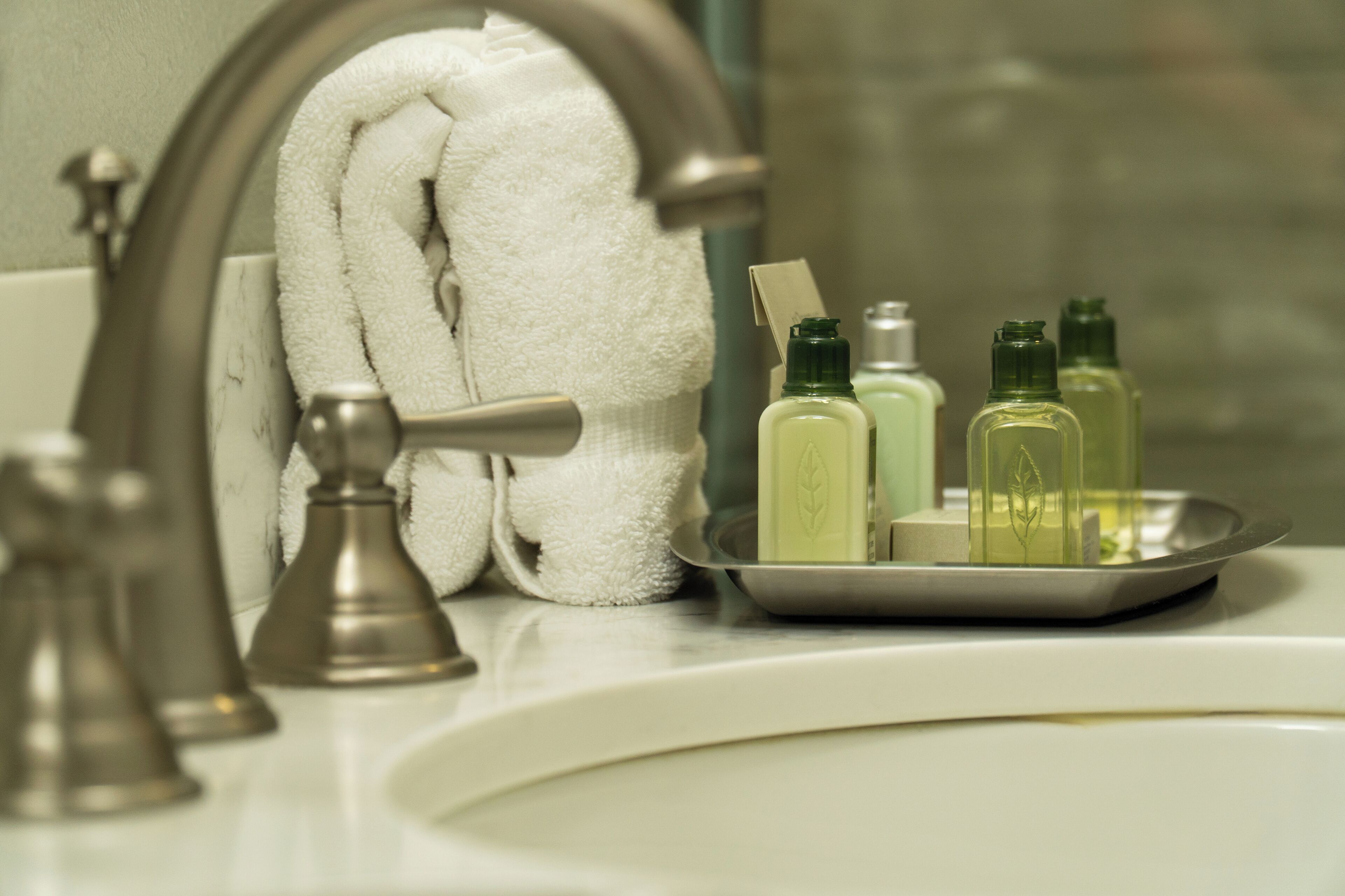A bathroom sink with a towel hanging on a towel rack, a soap dish with bottles, and a faucet.