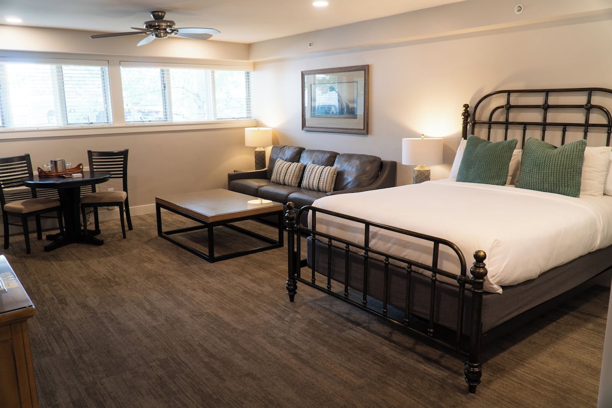 A bedroom with a bed, a sofa, a coffee table, and a desk with chairs.