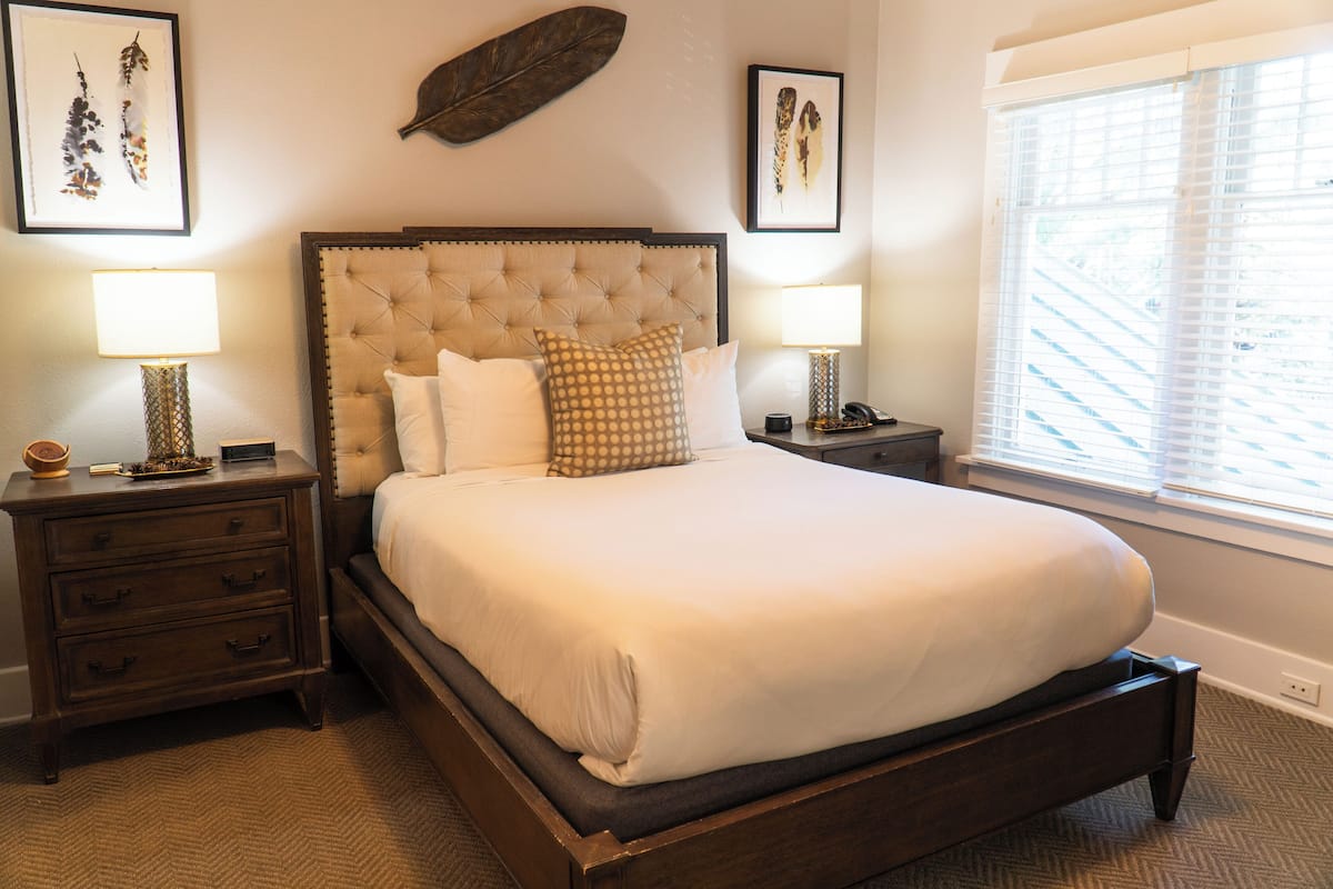 A large bed with a tufted headboard, two bedside tables with lamps, and artwork on the walls.