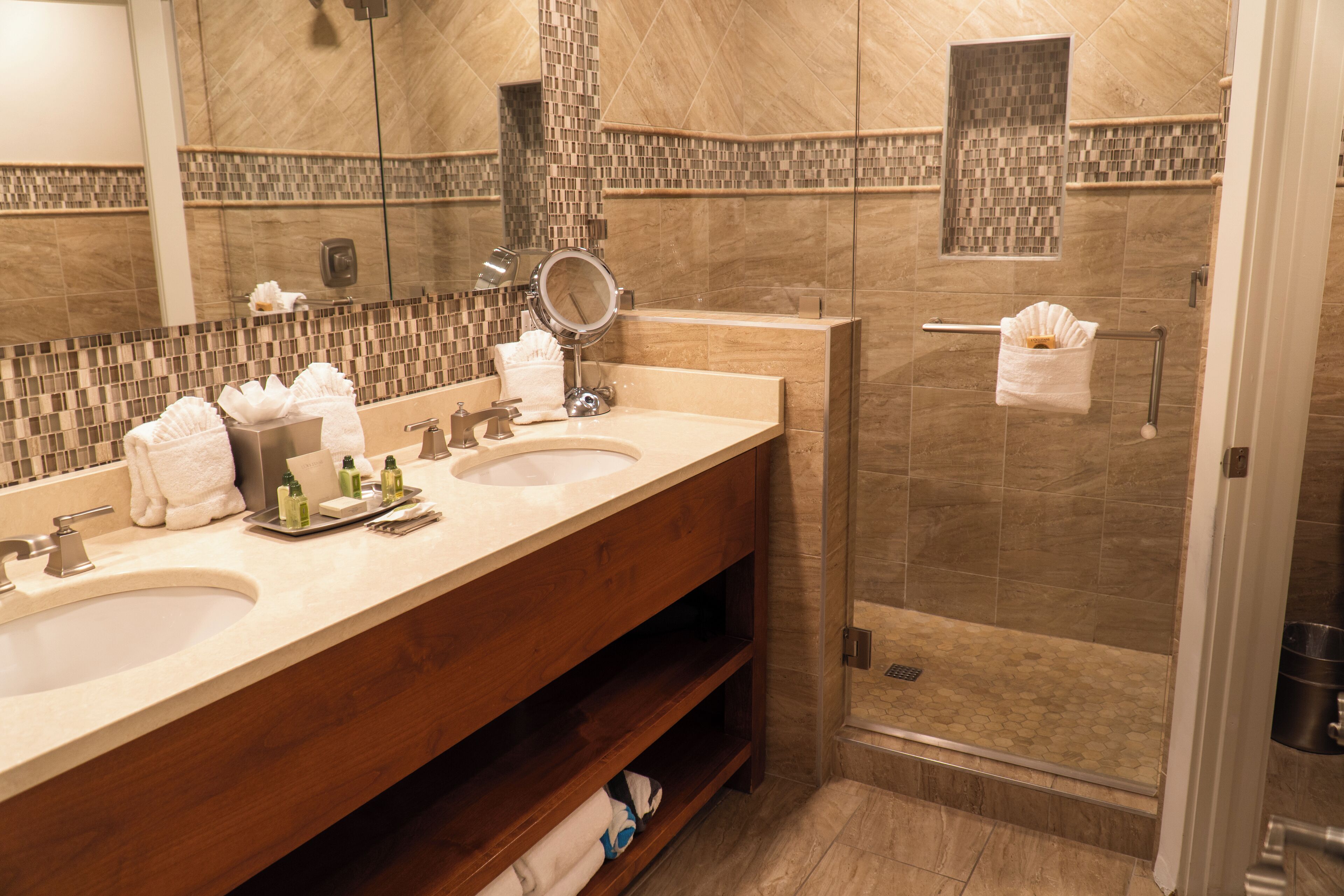 A modern bathroom with two sinks, a mirror, a shower, and a towel rack.