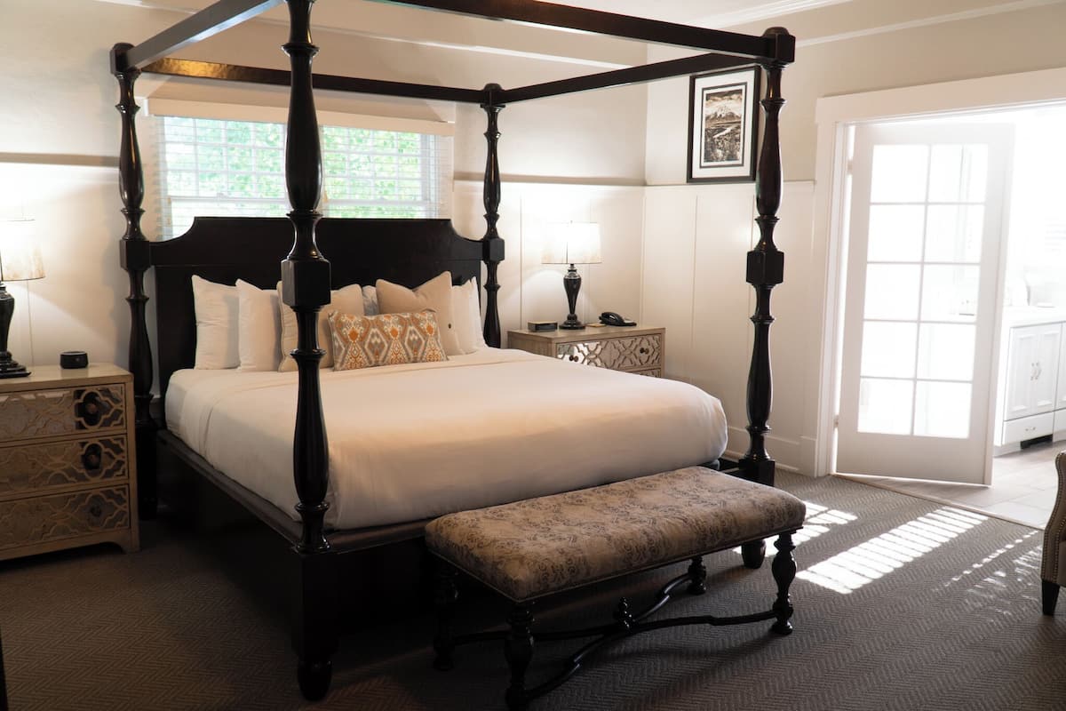 A four-poster bed with a matching bench, a bedside table with a lamp, and a framed picture on the wall.