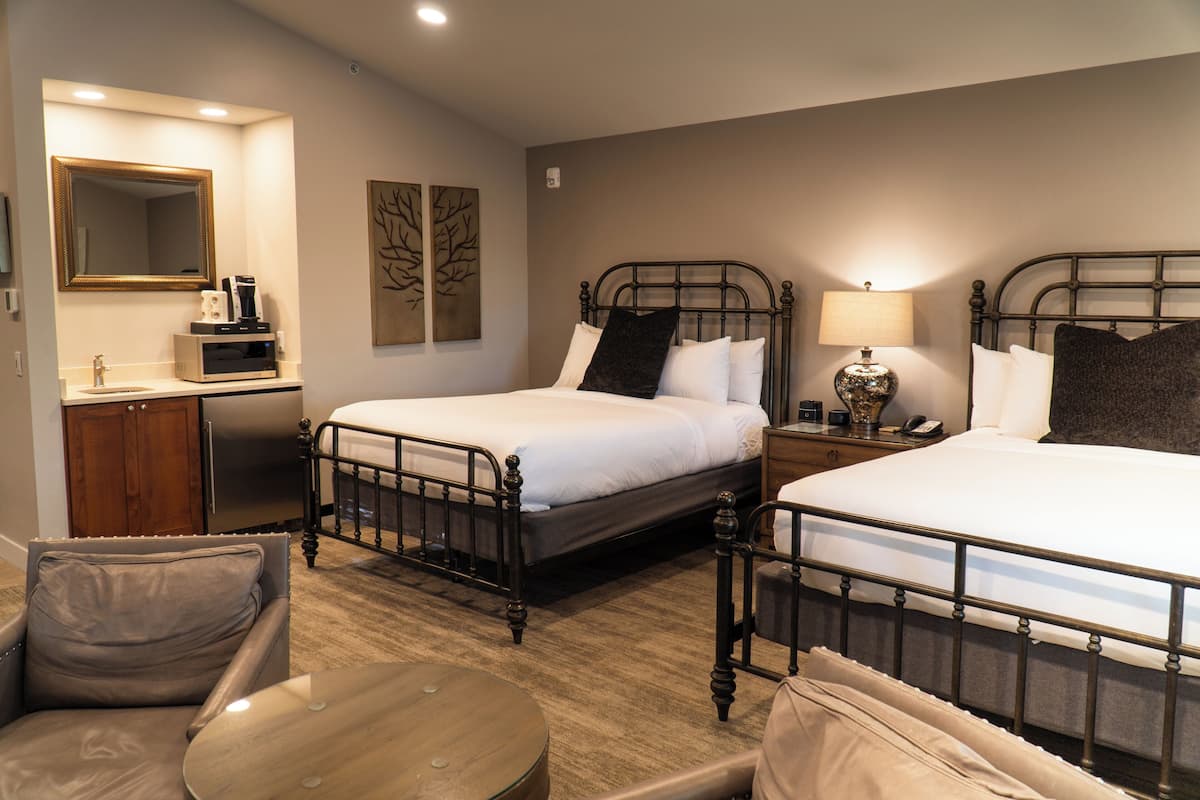 A hotel room with two beds, a desk with a mirror, a chair, and a round table.