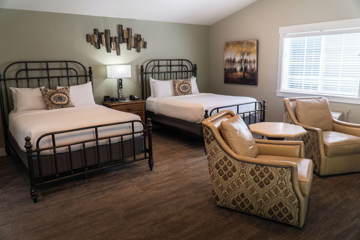 A hotel room with two beds, a sitting area with chairs, a lamp, and artwork on the walls.
