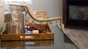A tray with glassware and a candle on a reflective surface, a patterned chair, and a fireplace in the background.