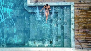 A person swimming in a rectangular pool with a wooden deck on one side. - Pousada Tororão (Porto Seguro)