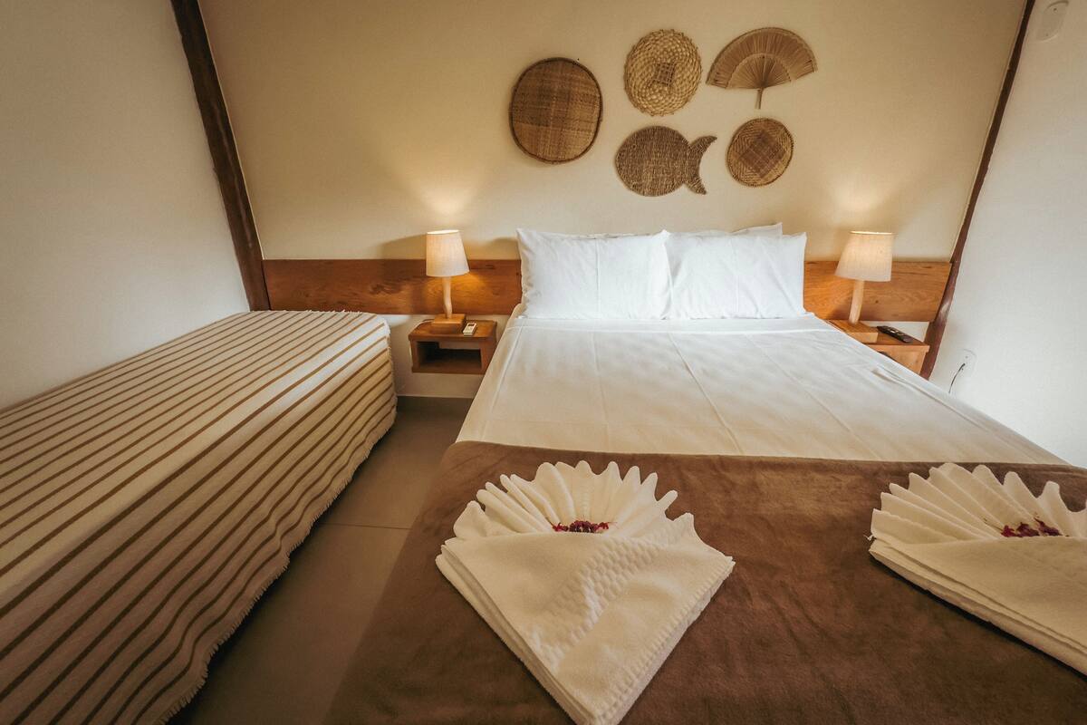 A hotel room with a large bed, two bedside tables, a nightstand, and a wall with decorative woven items.