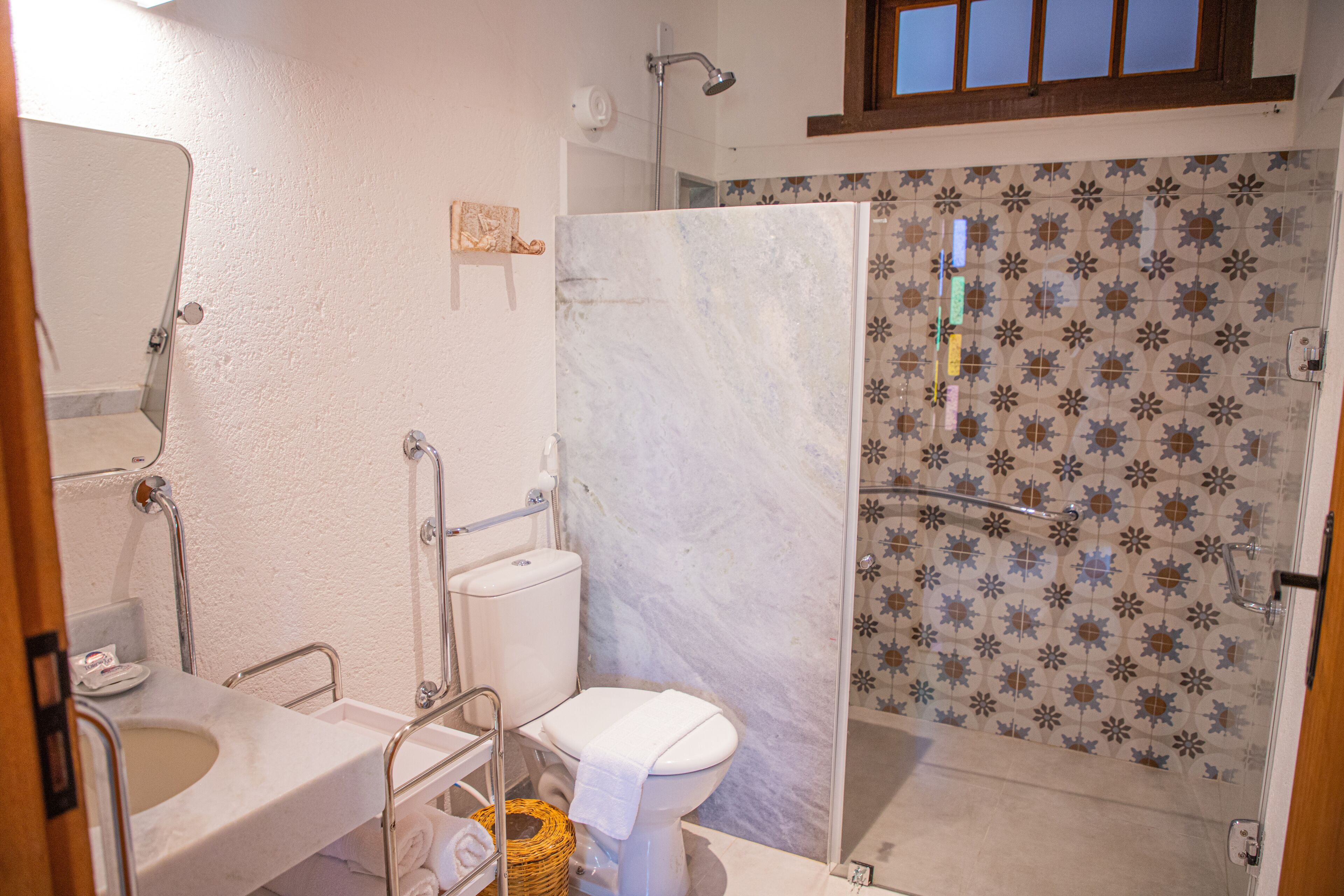 A bathroom with a white toilet, a sink, a shower with a glass door, and a patterned tile wall.