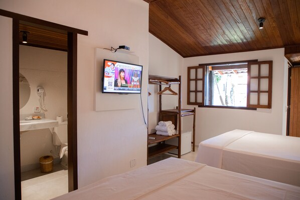 Quarto de hotel com duas camas, uma televisão fixada na parede, teto de madeira e um pequeno armário com toalhas.
