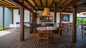 A wooden deck with a round table and chairs, a bench, and a painting on the wall. - Pousada Tororão (Porto Seguro)