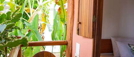 A wooden chair on a wooden deck, a bed with white bedding, and a wooden door leading to a room.