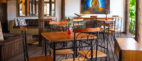 A wooden deck with tables and chairs, a sofa, and a painting on the wall.