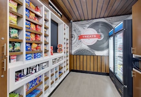 Pasillo con productos de snacks, estantes llenos de papas fritas y otros aperitivos, una sección refrigerada con bebidas y un letrero en la pared que indica la sección.