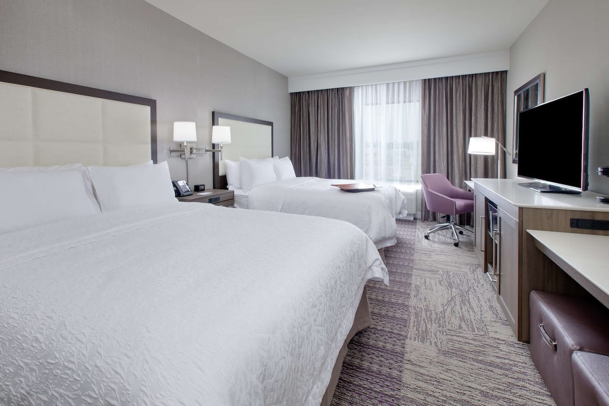 A hotel room with two beds, a desk, a chair, a television, and a window with curtains.