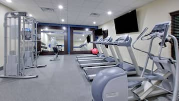 Un gimnasio con cintas de correr, elípticas y equipo de levantamiento de pesas.