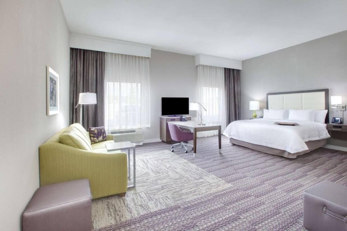 A hotel room with a bed, a desk, a chair, a sofa, and a television.