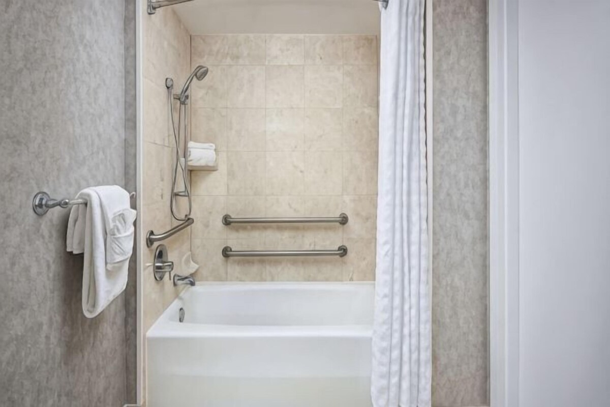 A bathroom with a bathtub, grab bars, a towel rack, and a shower head.