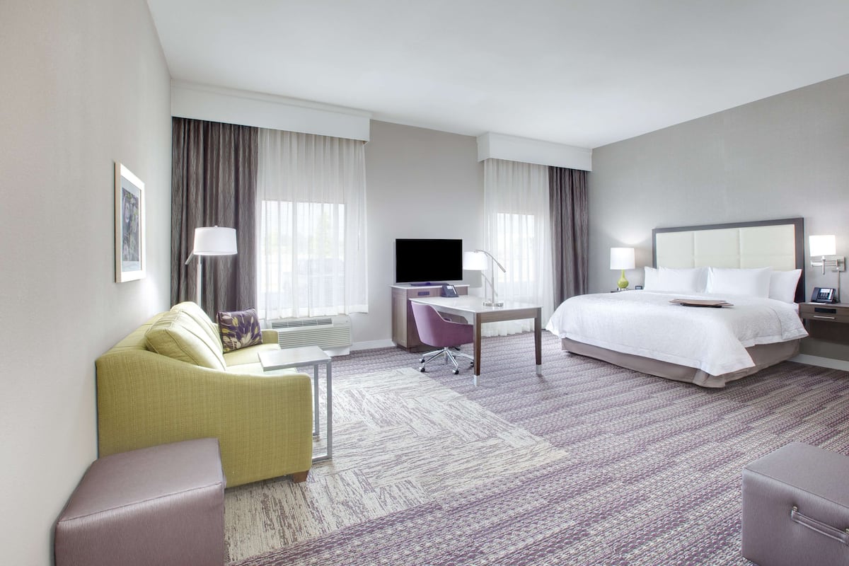 A hotel room with a bed, a desk with a computer, a sofa, and a chair.