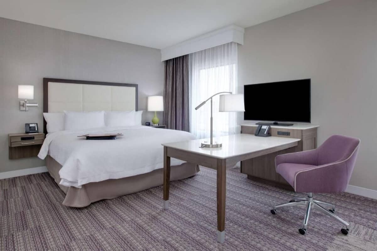 A hotel room with a bed, desk, chair, TV, and bedside lamps.