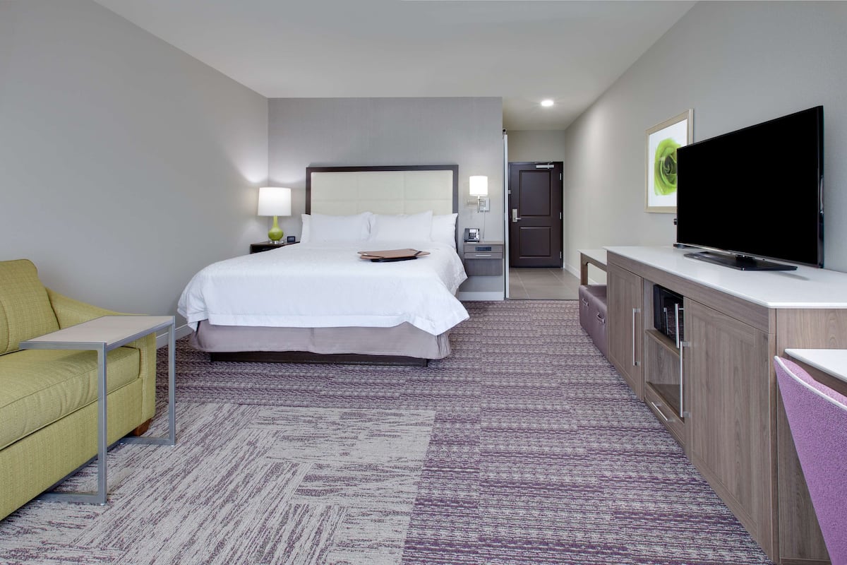 A hotel room with a bed, a television, a desk, a sofa, and a cabinet.