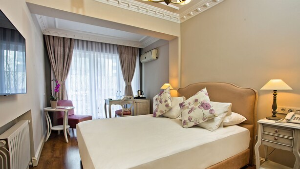 A hotel room with a large bed, a desk, a chair, a lamp, and a radiator. - Villa Blanche Hotel (Istanbul)