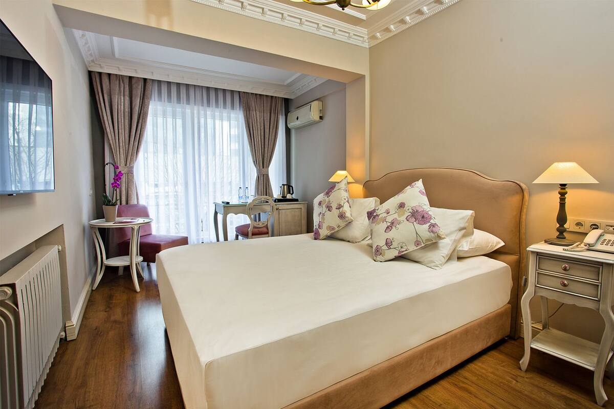 A hotel room with a large bed, a desk, a chair, a lamp, and a radiator.