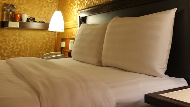 A hotel room with a bed, pillows, a nightstand, a lamp, and a phone. - Goodness Hotel (Kaohsiung)