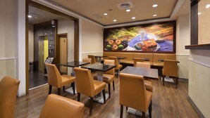 A restaurant with tables and chairs, a mural on the wall, and a door leading to another room. - Goodness Hotel (Kaohsiung)