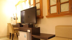 A compact living space with a flat-screen TV on a wooden stand, a small refrigerator, a beige sofa, and a dining table with chairs. - Goodness Hotel (Kaohsiung)