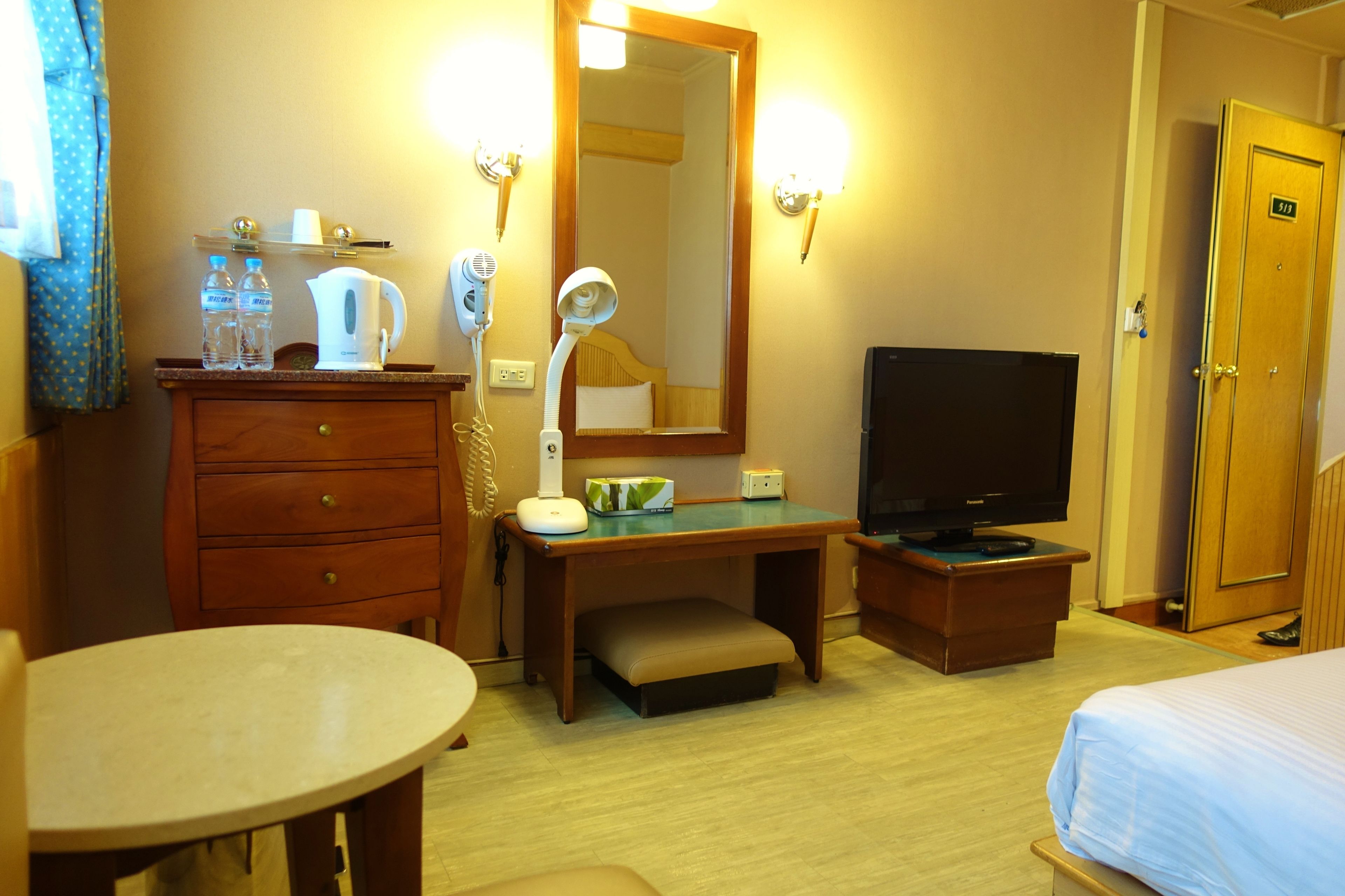 Una habitación de hotel con un escritorio de madera, televisor, espejo y cama.